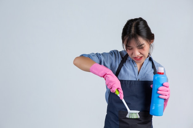 Young housewife is wearing yellow gloves while cleaning with the product of clean on white wall.