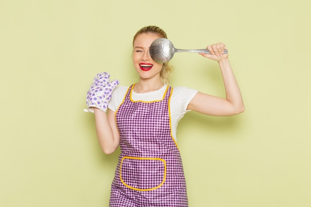 Free photo young housewife in shirt and colored cape holding sivler spoon on green