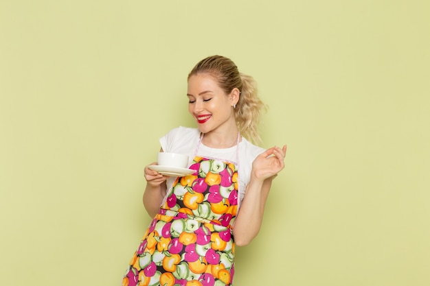 young housewife in shirt and colored cape holding white cup on green