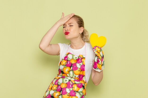 young housewife in shirt and colored cape holding yellow heart shape on green