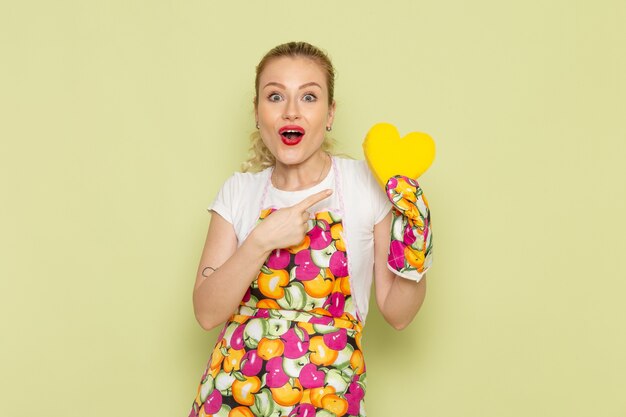 young housewife in shirt and colored cape holding yellow heart shape on green