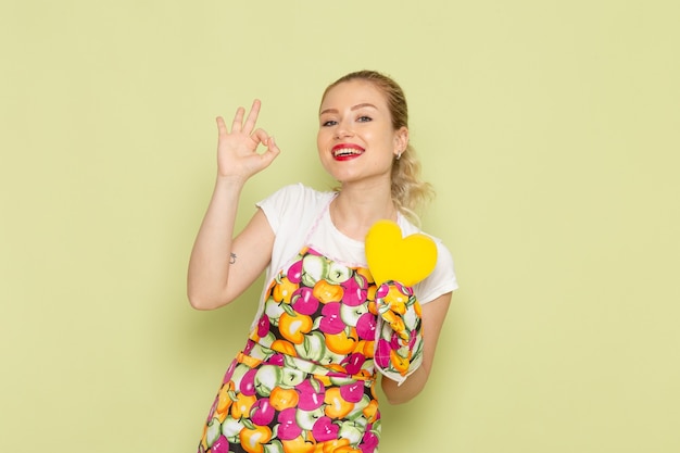 young housewife in shirt and colored cape holding yellow heart shape smiling on green