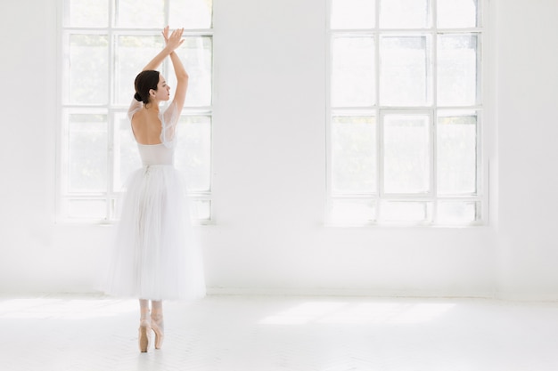 Young and incredibly beautiful ballerina is posing and dancing in a white studio