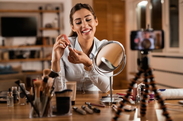 Free photo young influencer holding lip balm while vlogging about makeup at home