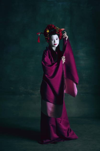 Young japanese woman as geisha on dark green