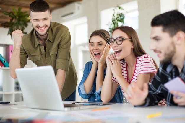 Young joyful business people happily working on laptop together Group of smiling men and women spending time in modern cozy office