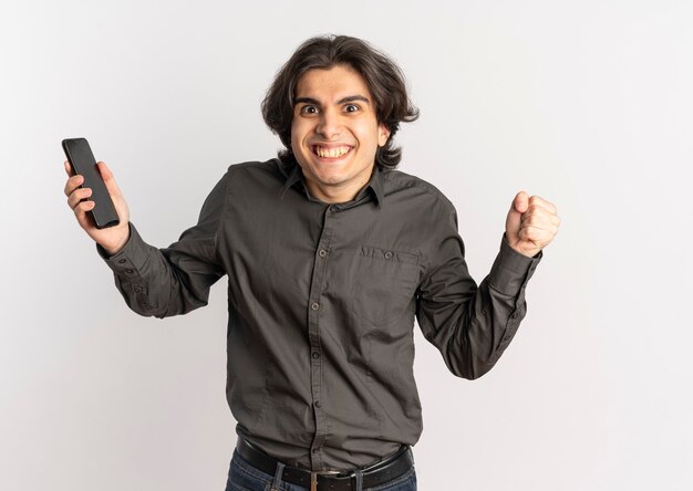 Young joyful handsome caucasian man holds phone and keeps fist up isolated on white background with copy space