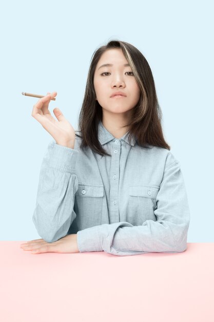 Young korean women smoking cigar while sitting at table at studio.