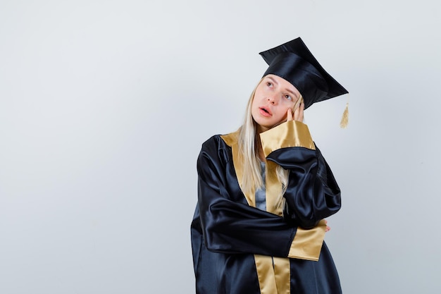 Young lady in academic dress standing in thinking pose and looking thoughtful