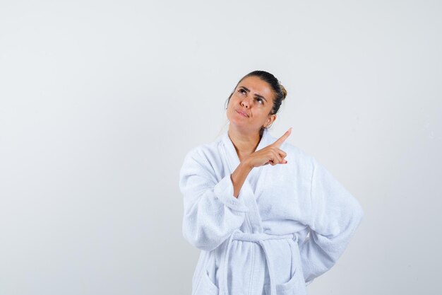 Young lady in bathrobe pointing aside and looking thoughtful