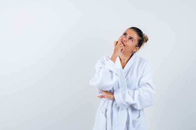 Free photo young lady in bathrobe standing in thinking pose and looking thoughtful