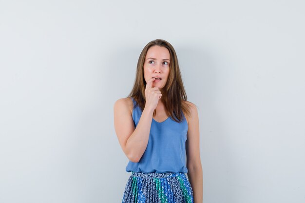 Young lady biting her nail in singlet, skirt and looking pensive