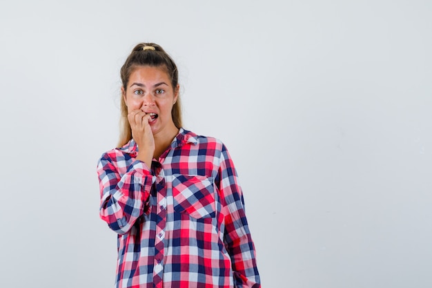 Free Photo young lady biting her nails in checked shirt and looking excited. front view.