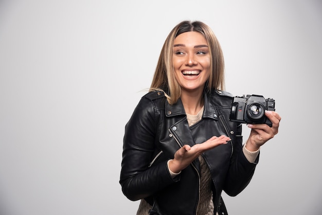 Young lady in black leather jacket taking photos with camera in a positive and smiling manner.