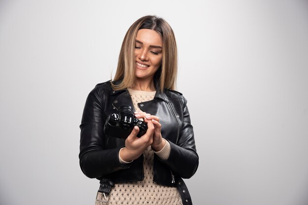 Young lady in black leather jacket taking photos with camera in a positive and smiling manner