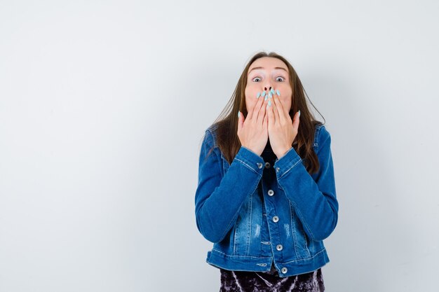 Young lady in blouse, denim jacket with hands on mouth to send kiss and looking cute , front view.