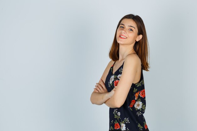 Young lady in blouse holding arms folded and looking cheerful .