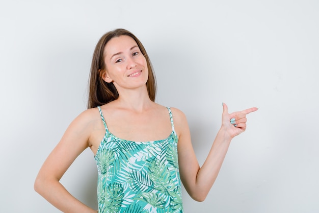 Young lady in blouse pointing to the right side and looking cheery , front view.