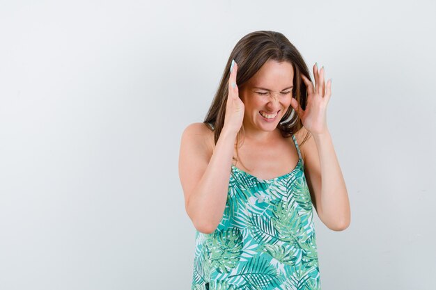 Young lady in blouse raising hands near head and looking annoyed , front view.