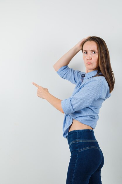 Young lady in blue shirt, pants pointing away and looking confused