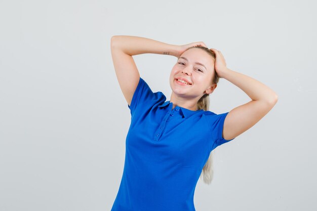 Young lady in blue t-shirt posing with hands on head and looking cheerful