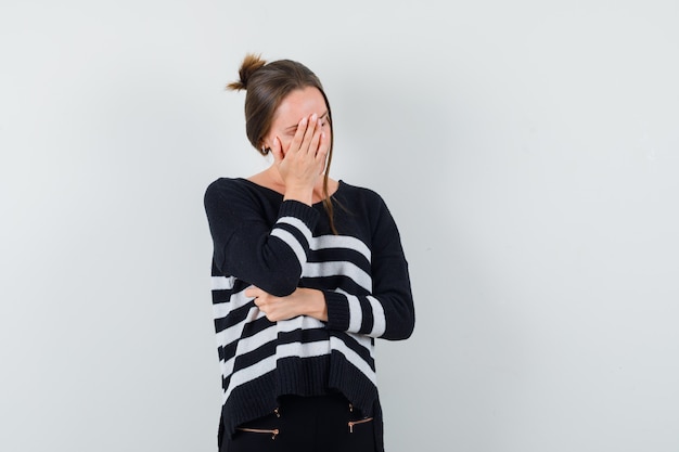 Young lady in casual shirt keeping hand on face and looking tired