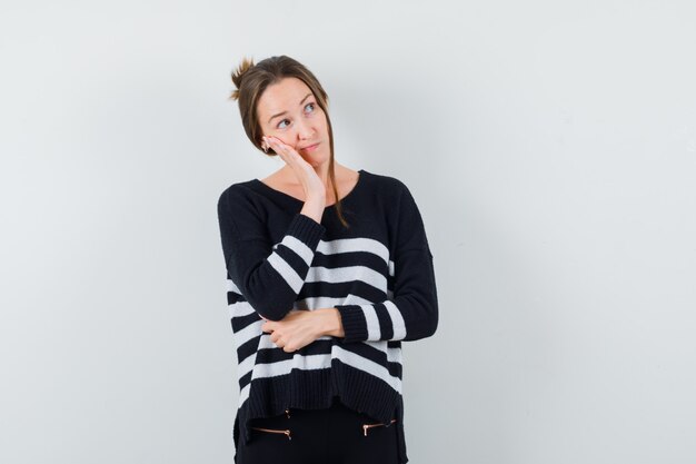 Young lady in casual shirt leaning cheek on palm and looking pensive