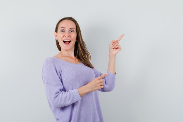 Young lady in casual shirt pointing at upper right corner and looking merry 