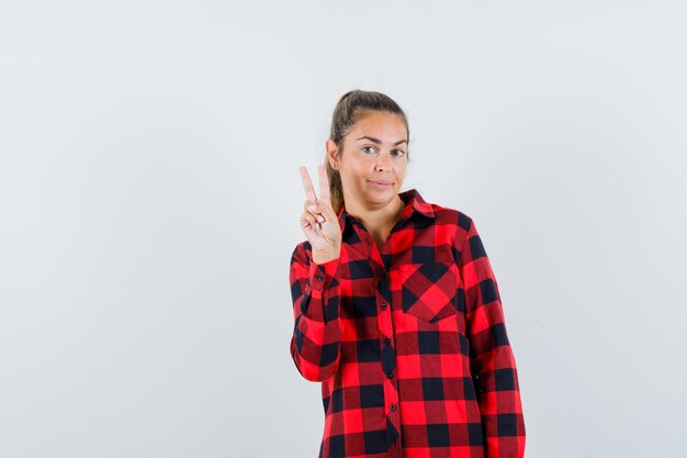 Young lady in casual shirt showing victory sign and looking confident , front view.