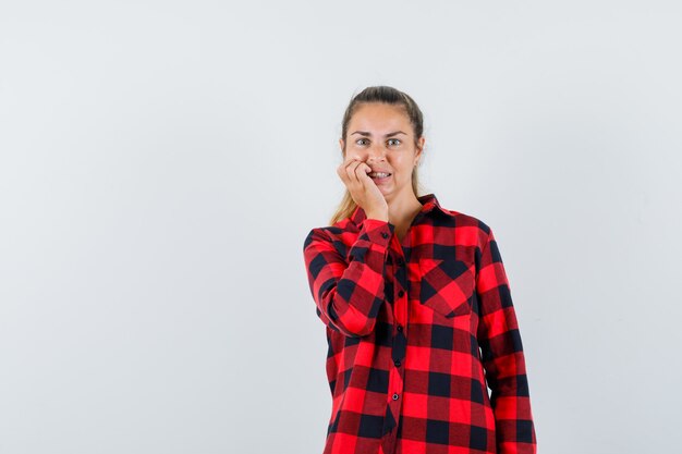 Young lady in casual shirt standing in thinking pose and looking anxious , front view.