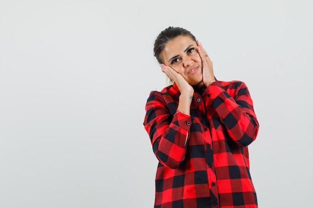 Young lady in checked shirt holding hands on cheeks and looking dreamy