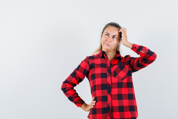 Young lady in checked shirt scratching head and looking hesitant