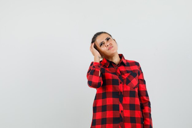 Young lady in checked shirt scratching head, looking up and looking pensive