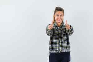 Free photo young lady in checked shirt showing double thumbs up and looking confident , front view.