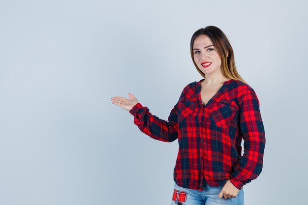 Young lady in checked shirt showing welcoming gesture and looking confident , front view.