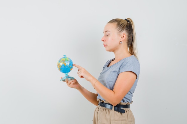 Young lady choosing destination on globe in t-shirt, pants and looking pensive.