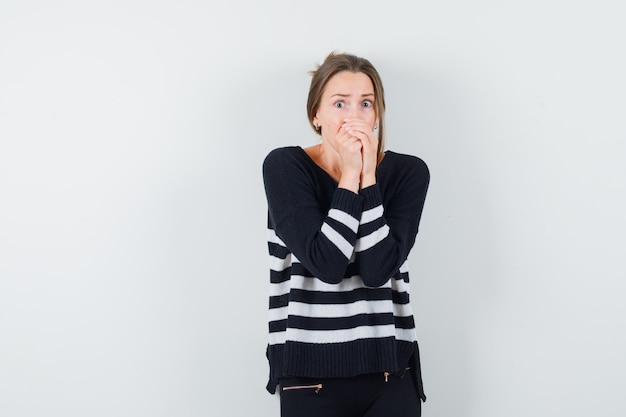 Young lady clasping hands on mouth in casual shirt and looking scared