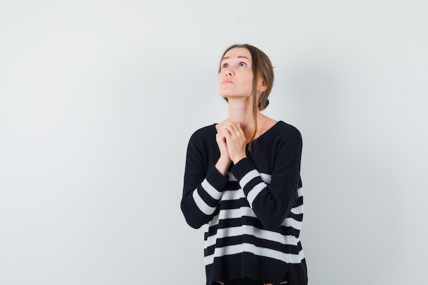 Free photo young lady clasping hands in praying gesture in casual shirt and looking hopeful