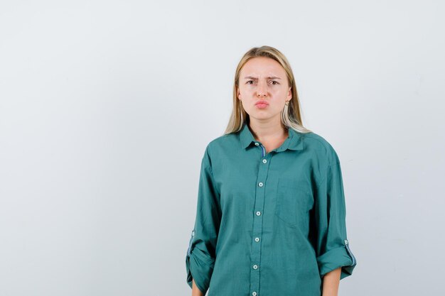 Young lady curving lips in green shirt and looking gloomy