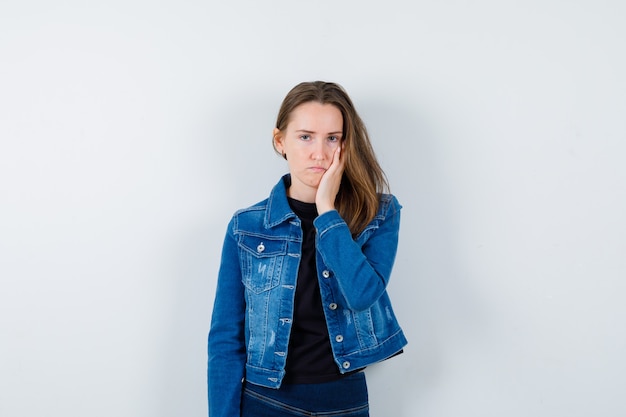 Young lady holding hand on cheek in blouse and looking sad, front view.