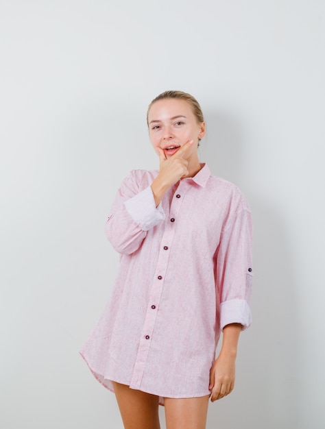 Free photo young lady holding hand on chin in pink shirt and looking pensive