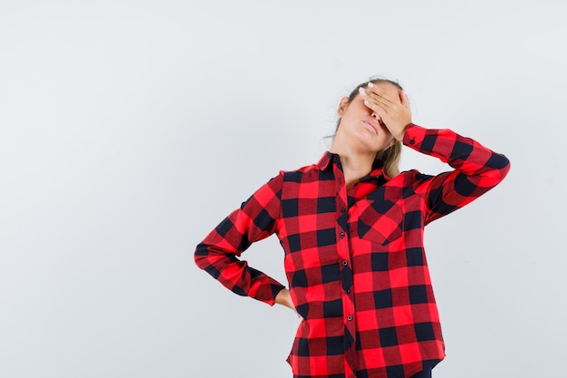 Young lady holding hand on eyes in checked shirt and looking calm