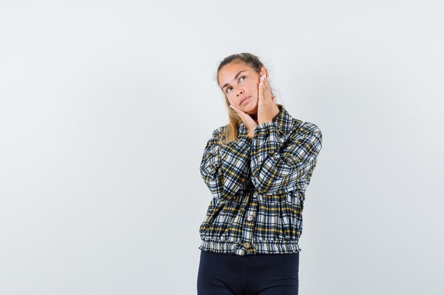 Young lady holding hands on cheeks in shirt, shorts and looking dreamy. front view.