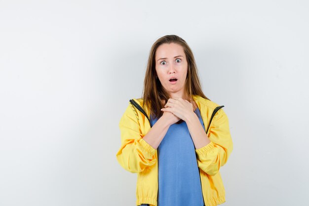 Young lady holding hands on chest in t-shirt and looking surprised