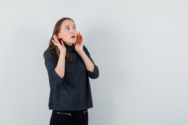 Young lady holding hands behind ears in shirt