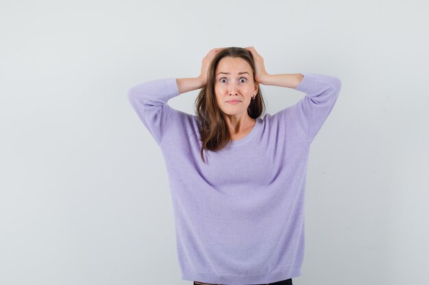 Young lady holding hands on head in casual shirt and looking helpless. front view.