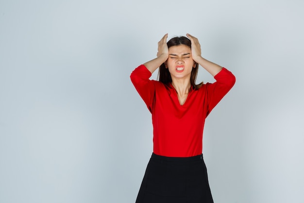 Free photo young lady holding hands on head in red blouse, skirt and looking exhausted