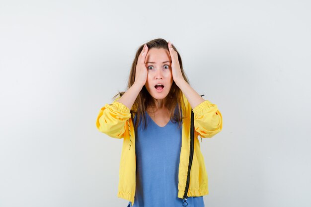 Young lady holding hands on head in t-shirt, jacket and looking wistful.