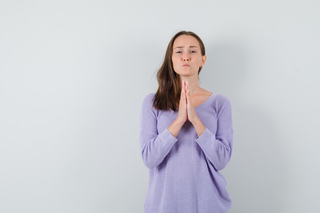 Young lady holding hands in praying gesture in casual shirt and looking hopeful 