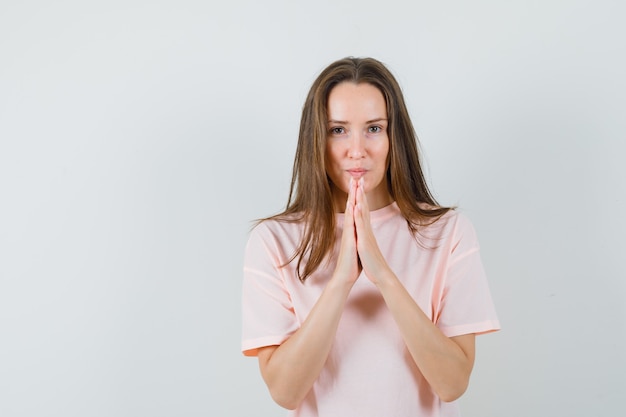 Free photo young lady holding hands in praying gesture in pink t-shirt and looking hopeful